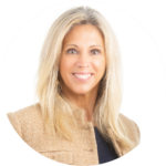 Makler Uschi-Baurecht mit langen blonden Haaren trägt eine beige Jacke über einem dunklen Oberteil vor weißem Hintergrund