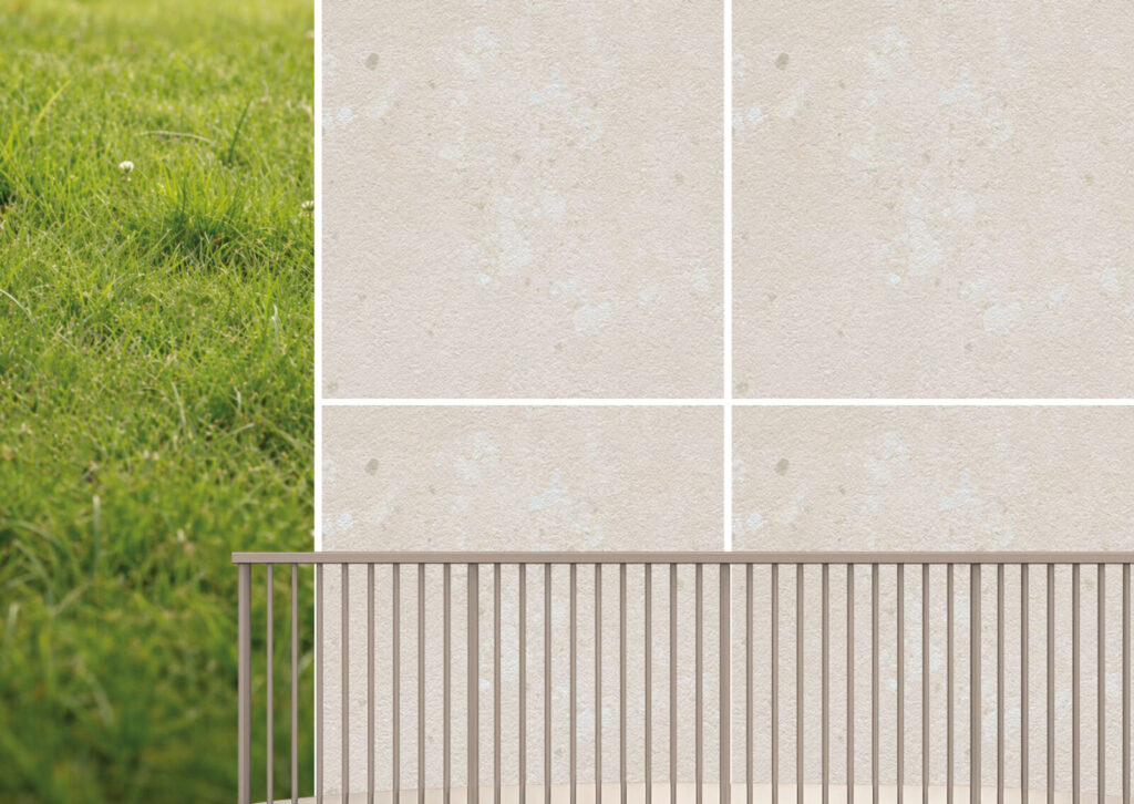 Glatt strukturierte, helle quadratische Fliesen und einem schlichten Metallzaun davor, links angrenzend an eine grüne Wiese.